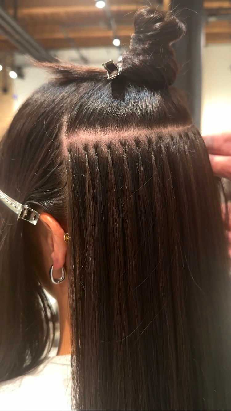 Hair extensions being applied to long, dark hair with clips and expert technique.